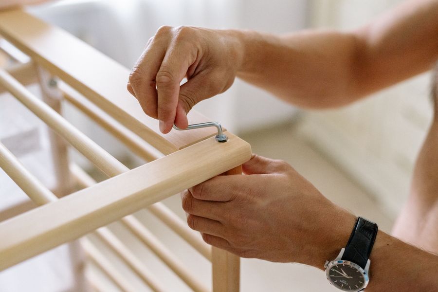 Hands tightening a bolt with an Allen key on a wooden crib frame