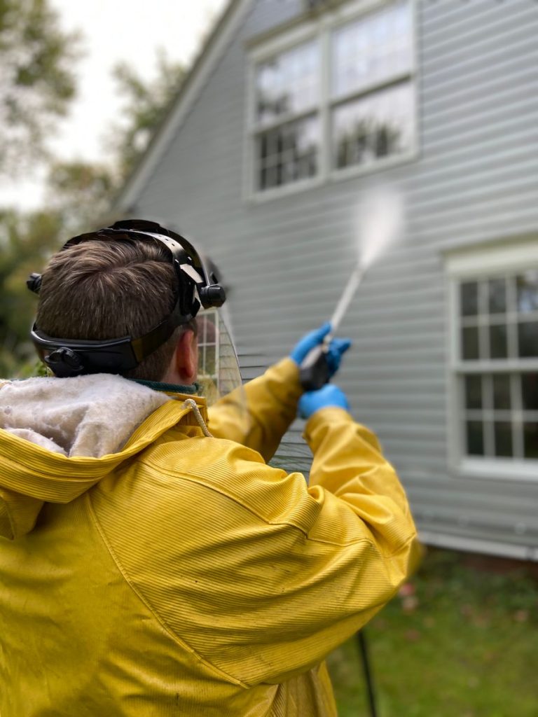 Person in a yellow rain jacket pressure washing the siding of a house